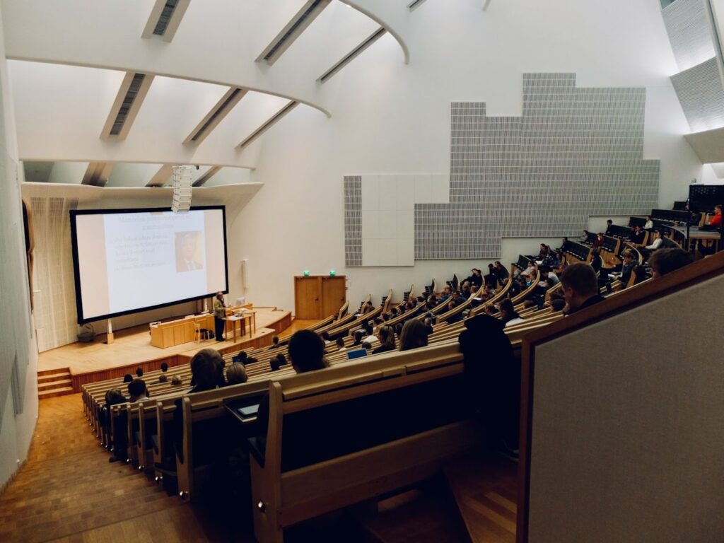 Students sit in a lecture hall while a professor lectures.