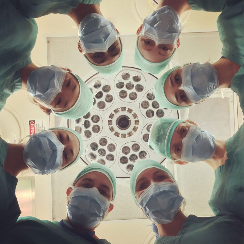 A group of medical professionals stand in a circle wearing green scrubs and face masks.