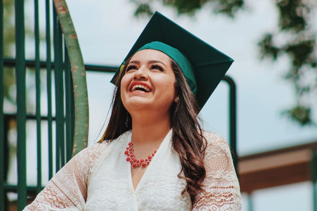 A woman stands and smiles while wearing a green graduation cap.