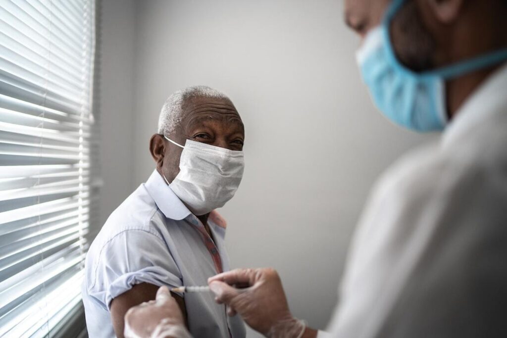 A health care practitioner gives an elderly patient in a mask a vaccination.
